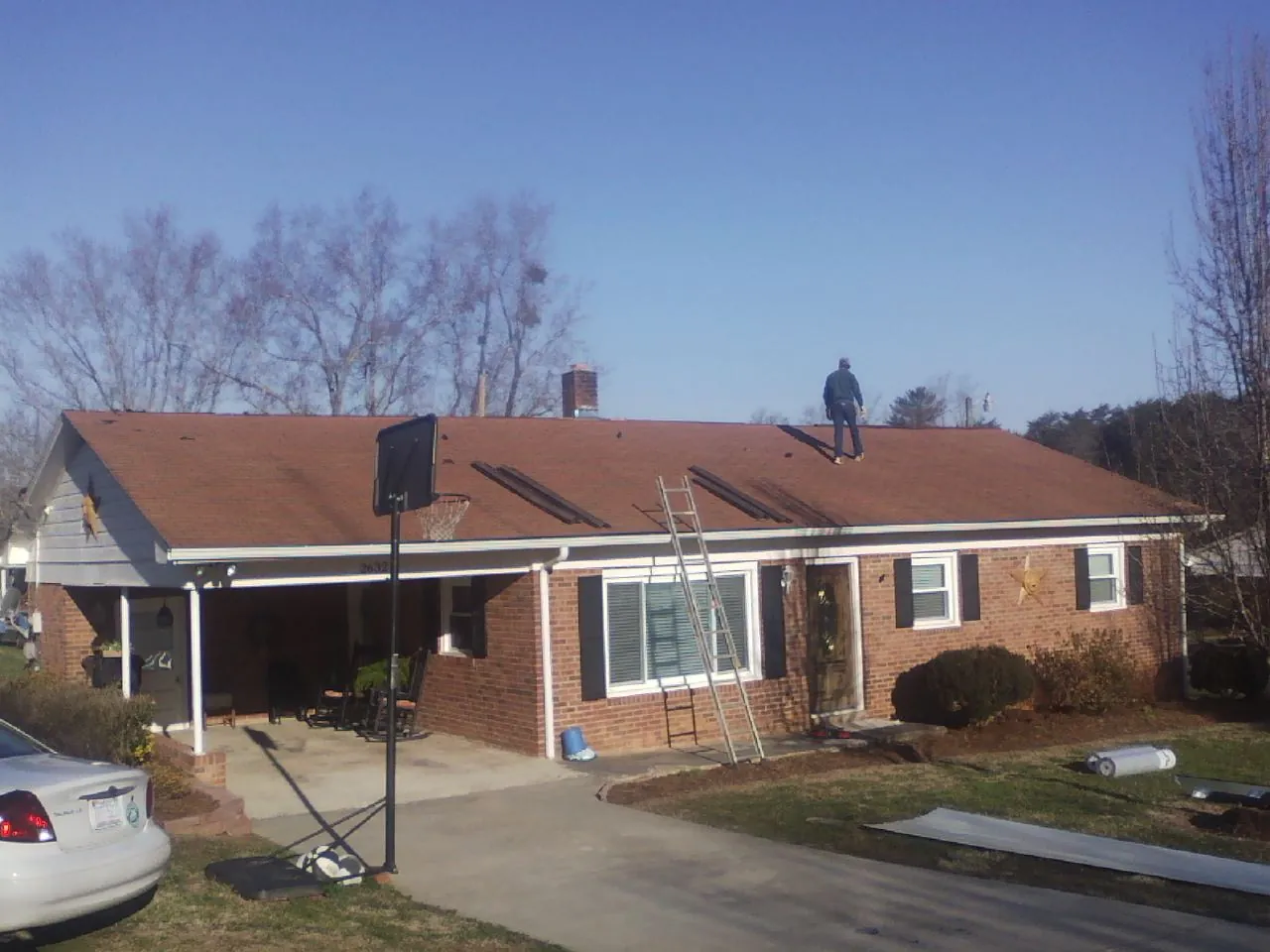 Roofer stripping a shingle roof on a brick ranch before metal panels in Dixon