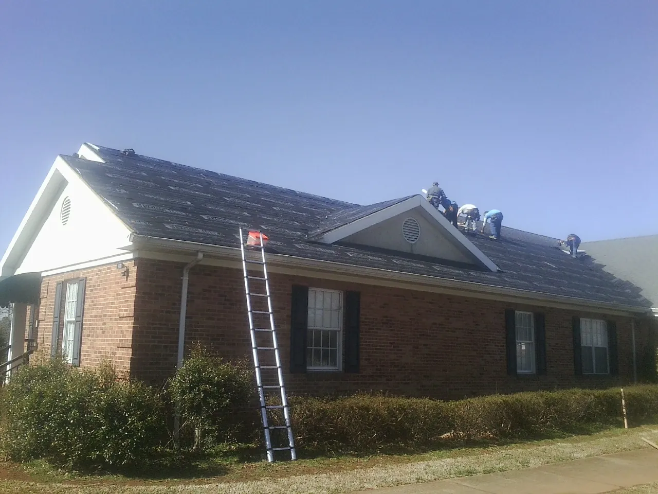 Crew tearing shingles off a brick ranch roof with a ladder set — Emergency Roof Repair work by our crew in Dixon